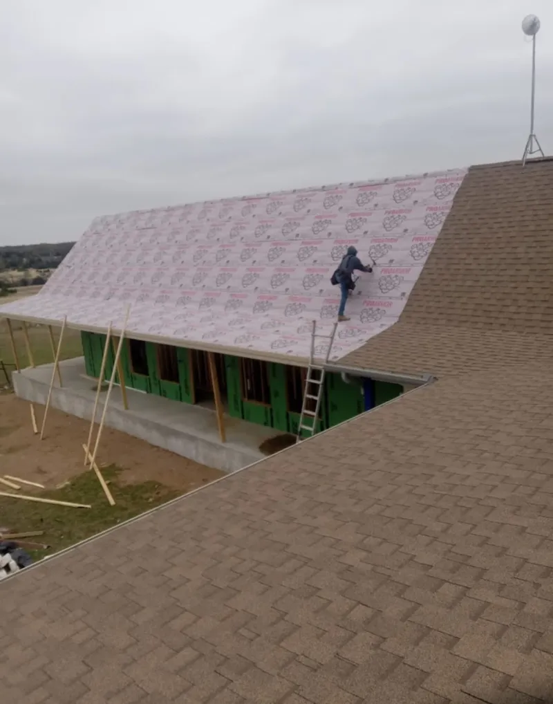 Worker preparing underlayment for a metal roof installation in Sienna